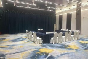Un salón de conferencias con escenario, una mesa larga y sillas dispuestas alrededor.