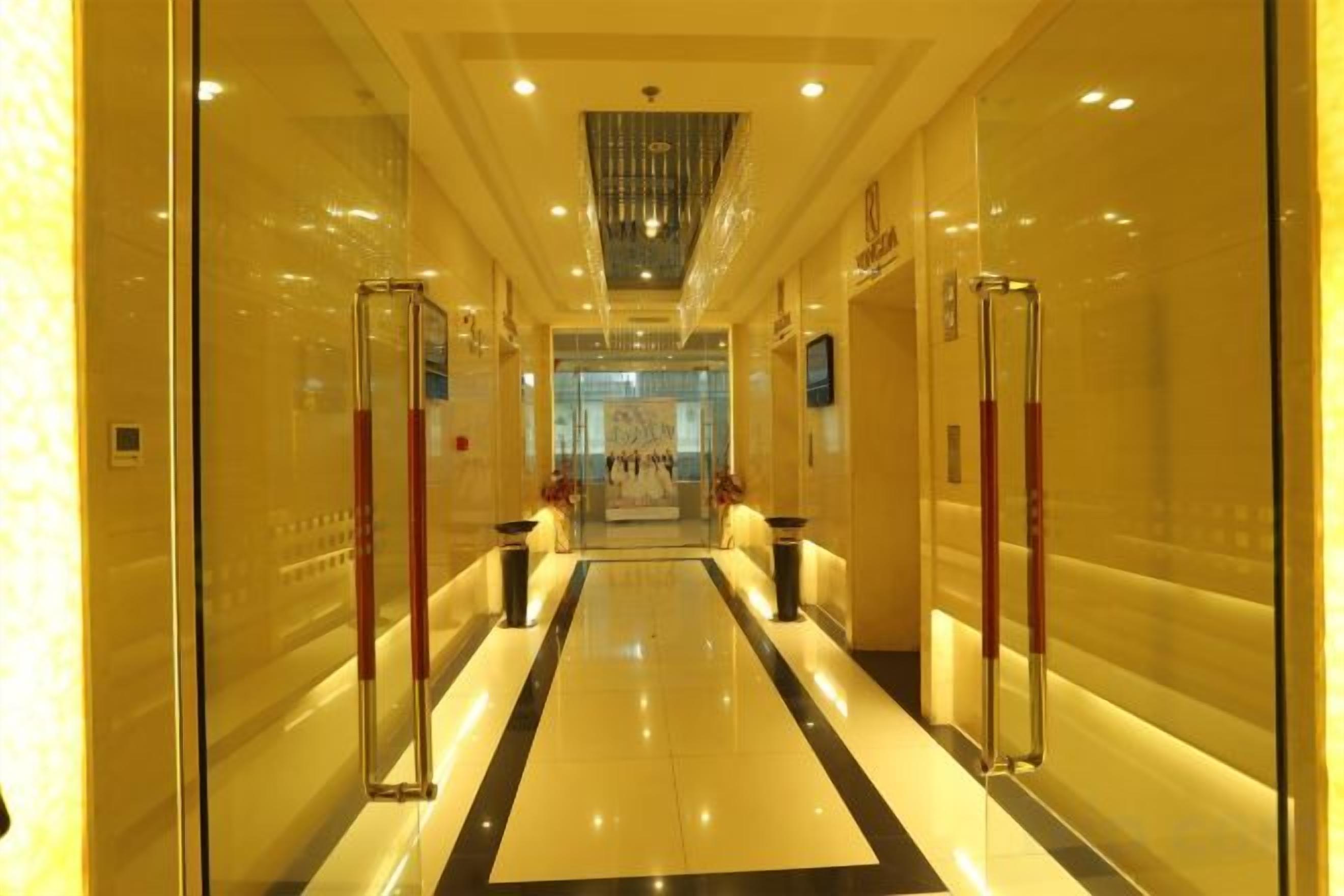 A hotel corridor with glass doors, a central light fixture, and a polished floor.