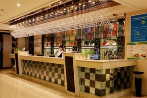 Ein Hotel-Rezeptionsbereich mit Schachbrettmuster-Boden, einer Angestellten hinter dem Empfangstresen und einer Speisekarte an der Wand.