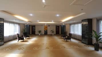 A spacious hotel lobby with a patterned carpet, seating arrangements, and potted plants.