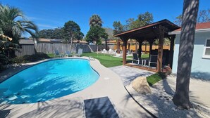 Un patio trasero con piscina, un porche cubierto y una cerca de madera.