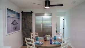 Un comedor con una mesa de madera, sillas blancas y un refrigerador moderno.