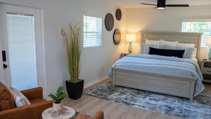 Un dormitorio con cama, mesitas de noche, ventilador de techo y una planta en maceta.