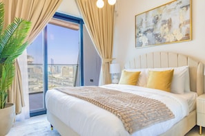 A hotel room with a large bed, a view of the city, and a potted plant.