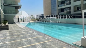 A modern residential building with a swimming pool, balconies, and a clear sky.