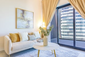 A modern living room with a white sofa, a round coffee table, and a large window with curtains.