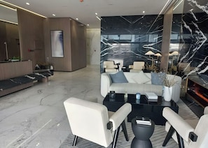 A modern hotel lobby with a reception desk, seating area, and a large marble wall.