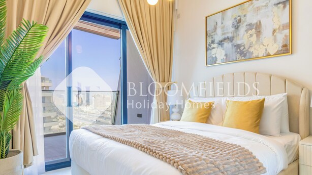 A bedroom with a large bed, a potted plant, a view of the city, and a painting on the wall.