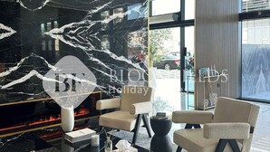 A modern hotel lobby with a black marble fireplace, comfortable seating, and a large window offering a view of the street.