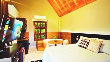A bedroom with a wooden ceiling, a bed with white bedding, a desk with a computer, and a small table with chairs.