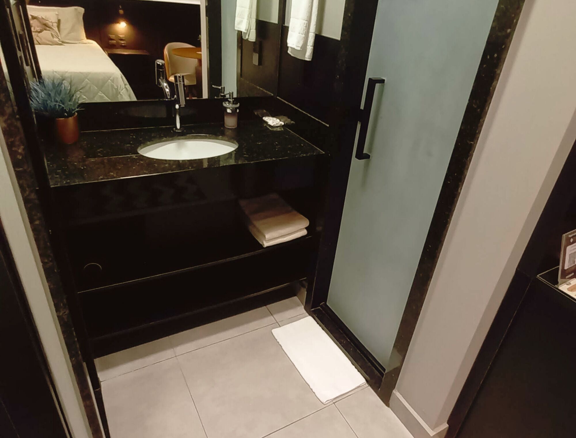 Casa de banho compacta com bancada preta, lavatório branco e suporte de toalhas.