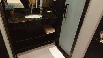 Casa de banho compacta com bancada preta, lavatório branco e suporte de toalhas.