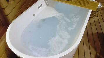 Una bañera llena de agua, suelo de madera y una botella de vino sobre una estantería de madera.