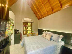A bedroom with a large bed, a wooden ceiling, a small table with a plant, and a wall-mounted TV. - Villaggio dos Vinhedos (Garibaldi)