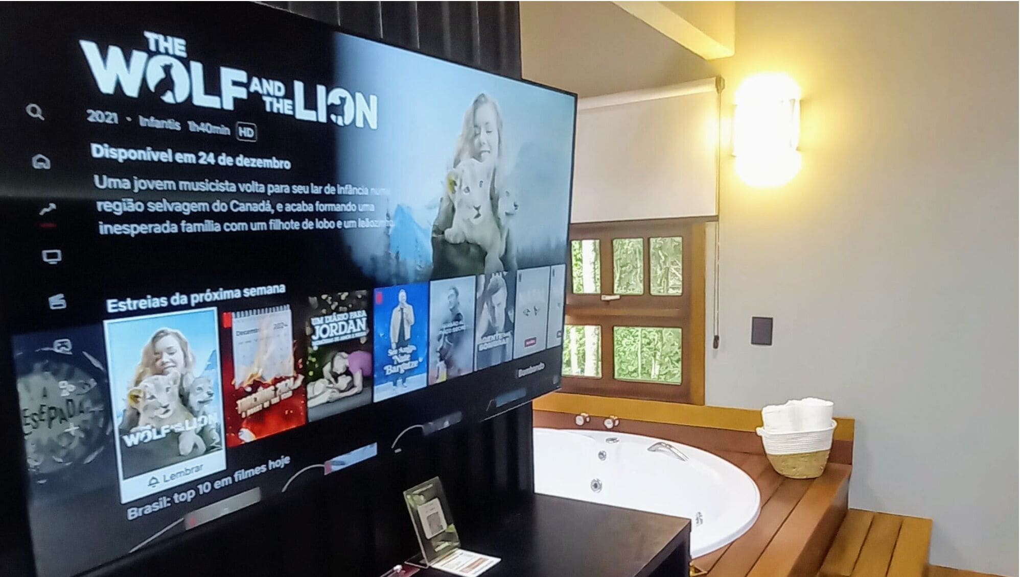 Un televisor mostrando la película 'El Lobo y el León', una bañera y un piso de madera en una habitación.