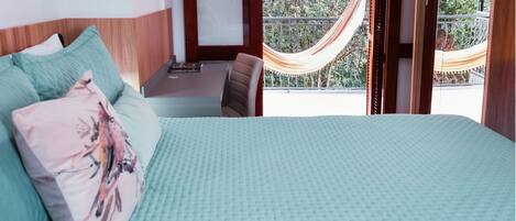 Un dormitorio con cama, almohadas, un escritorio y una hamaca fuera de la ventana.