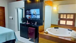 A modern bathroom with a large bathtub, a vanity with a mirror, and a television mounted on the wall displaying a movie. - Villaggio dos Vinhedos (Garibaldi)