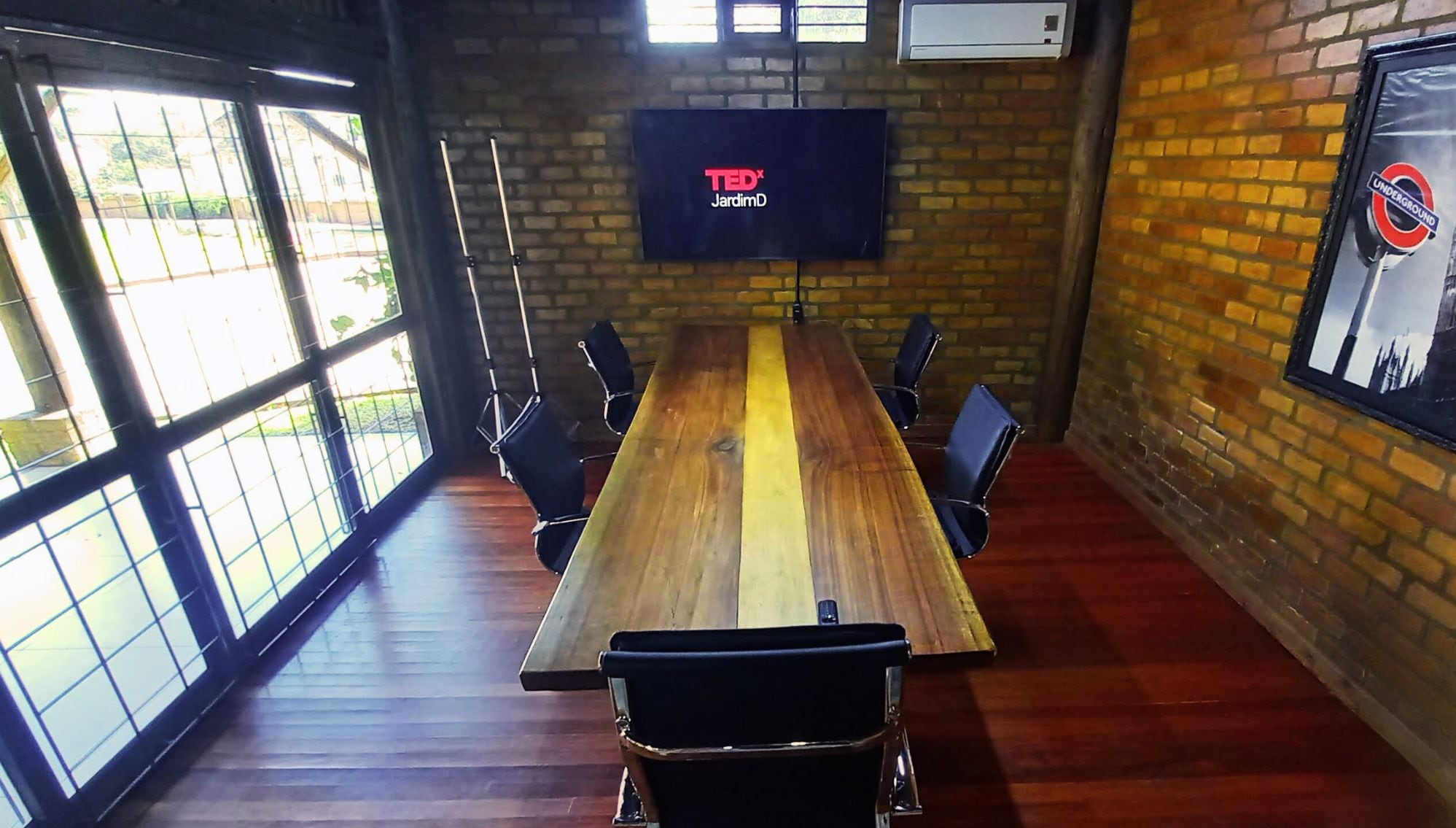 Une salle de conférence avec une longue table en bois, des chaises noires, un écran de télévision et un mur en briques.