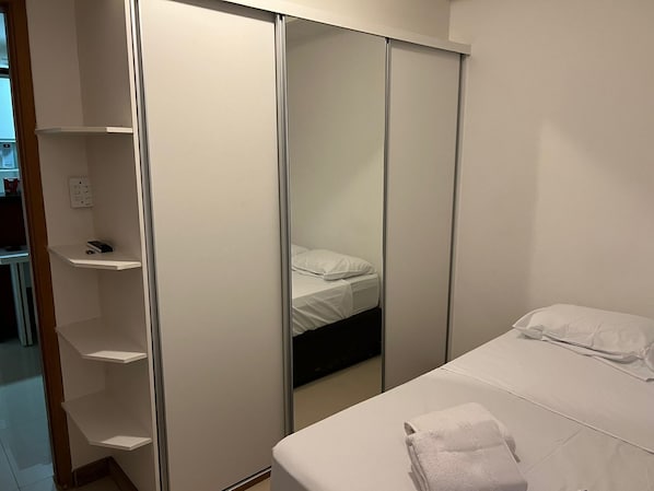 A bedroom with a bed, a white towel, and a wardrobe with a mirror.