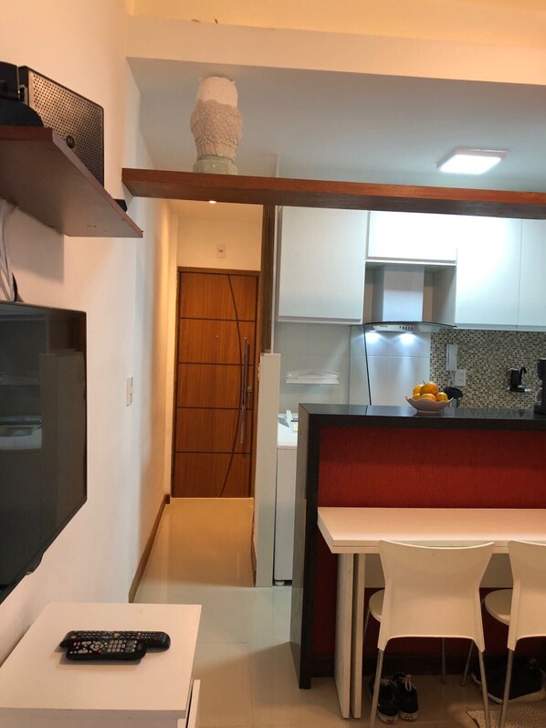 A compact kitchen with a microwave, a small refrigerator, and a sink. There is a wooden door leading to another room, and a white table with chairs.