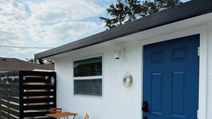 A small building with a blue door, a window with blinds, and a small table with chairs outside.