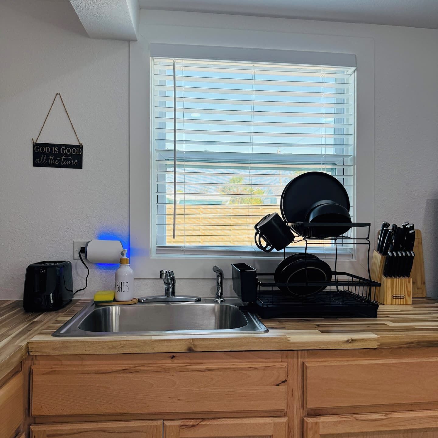 A kitchen with a stainless steel sink, a dish rack, and a window with blinds.
