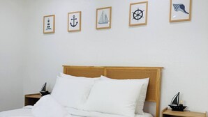 A neatly made bed with white linens, a wooden headboard, and a wall with nautical-themed artwork.