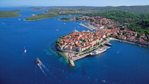 Vue aérienne d’une ville côtière avec un port, des bateaux et la végétation environnante.