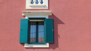 Un immeuble à la façade rouge, doté d’un balcon avec des balustrades blanches et d’une fenêtre avec des volets verts.