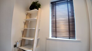 A room with a white wall, a window with horizontal blinds, and a wooden ladder shelf unit against the wall. - Stylish Stay in Vibrant Salford, Manchester! (Salford)
