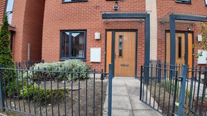 A brick building with a wooden door marked with the number 15, a small window, and a metal gate. - Stylish Stay in Vibrant Salford, Manchester! (Salford)