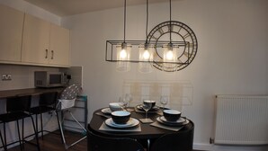 A modern kitchen with a dining area, featuring a round table set for four with plates, bowls, and wine glasses. - Stylish Stay in Vibrant Salford, Manchester! (Salford)