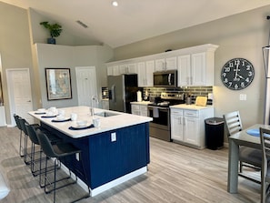 A modern kitchen with a central island, white cabinetry, stainless steel appliances, and a large wall clock.