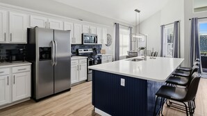 Una cocina moderna con armarios blancos, electrodomésticos de acero inoxidable, una isla grande y vistas al exterior.