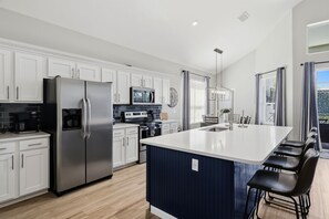 Una cocina moderna con armarios blancos, electrodomésticos de acero inoxidable, una isla grande y vistas al exterior.