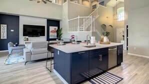Una cocina moderna con una isla central, una zona de comedor con sofá y una escalera que lleva a un nivel superior.