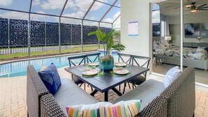 Un área junto a la piscina con una mesa dispuesta para comer, una planta en maceta y vistas a la piscina.