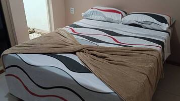 A bed with a patterned bedspread and a brown blanket, a white wall, and a door leading outside.