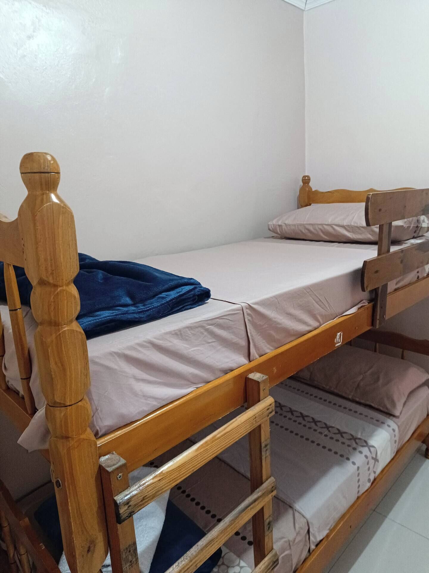 A bunk bed with a wooden frame and a blue blanket on the lower bunk.