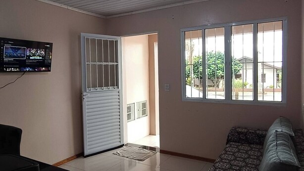 Una sala de estar con sofá, televisor montado en la pared, puerta con ventanal y suelo de baldosas.