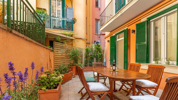 A patio with a wooden table and chairs, surrounded by potted plants and flowers. - Vatican Museums Stay with Terrace (Roma)