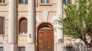A building with a central entrance featuring two wooden doors, flanked by white columns, and a plaque on the right. - Vatican Museums Stay with Terrace (Roma)