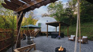 Un espace extérieur accueillant avec un foyer, des meubles en bois et un belvédère couvert.