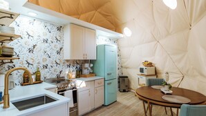 Une cuisine compacte équipée d’une cuisinière, d’un évier et d’un réfrigérateur. On y trouve une table à manger avec des chaises, et une petite plante est posée sur la table.