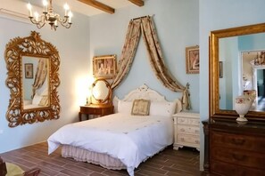 Een slaapkamer met een groot bed, een kroonluchter, een spiegel en een kast.