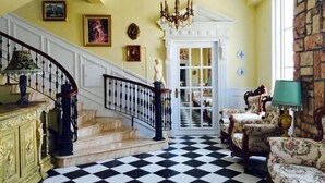 A staircase with a black and white checkered floor, a chandelier, and a door leading to another room.