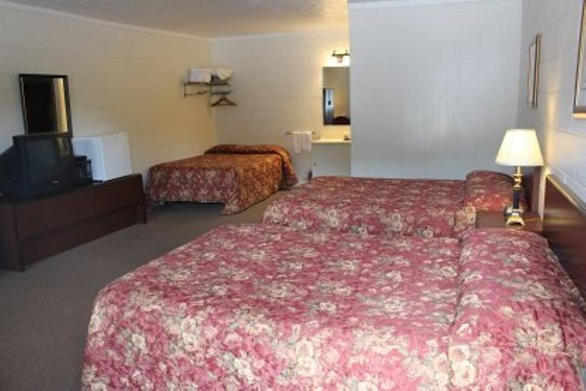 A hotel room with a large bed, a smaller bed, a desk, a TV, and a lamp.
