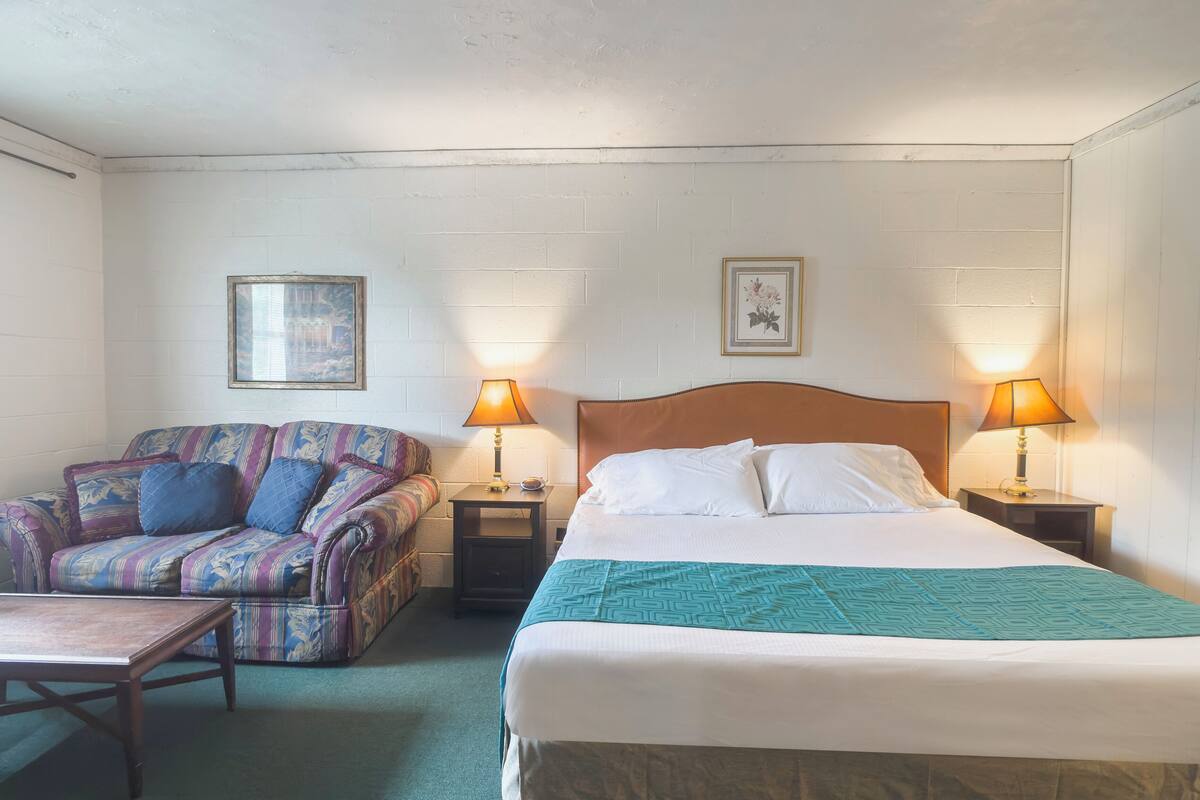 A hotel room with a bed, a sofa, two nightstands with lamps, and a small table.