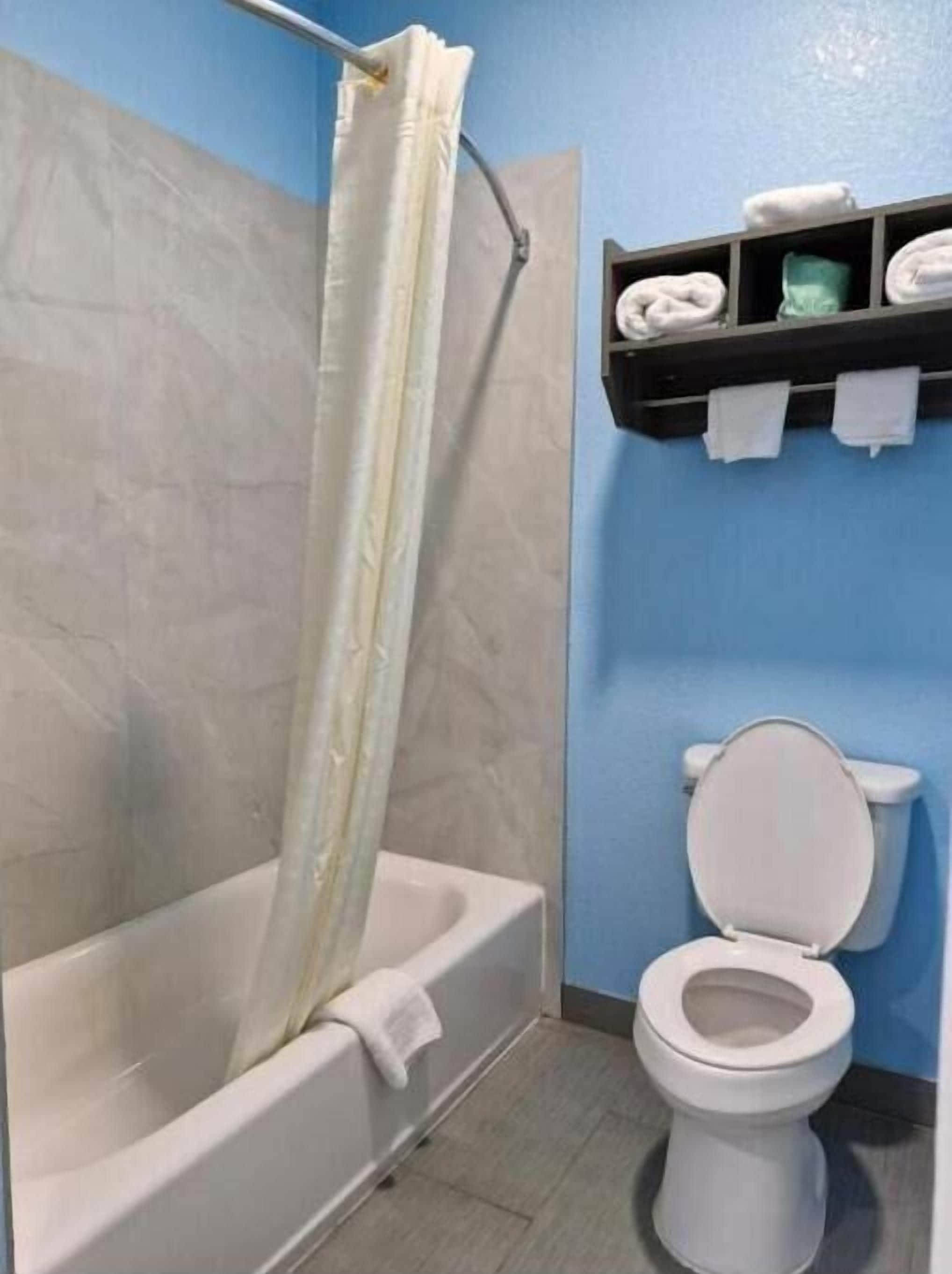 A bathroom with a bathtub, a toilet, and a shelf with towels.