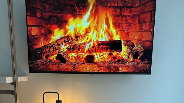 A room with a TV displaying a fireplace, a desk with a lamp, and a phone charging station. - Room25 InCentro Guest House (Cercola)
